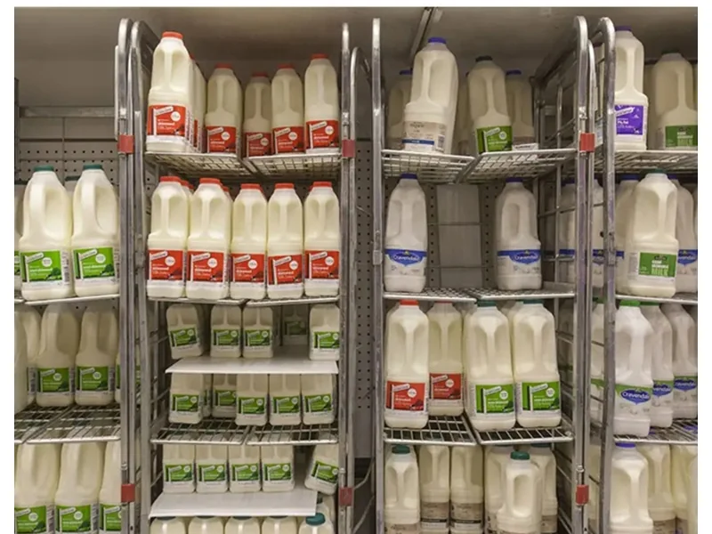 Milk bottles on the mesh shelves of milk trolleys in a store chiller